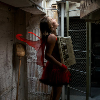Fine Art photographer David Lee Black portrait of Meghan Kallman with accordian, red wings near ladder of Superman Building, Providence, Rhode Island. Abandoned spaces. 